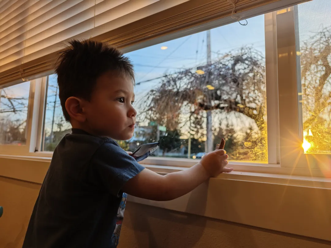 照片中，一个小孩站在窗边，框架的一角有太阳星