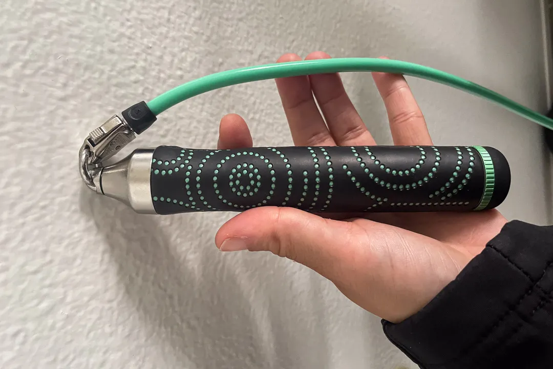 一只手握着一组黑色跳绳手柄，上面有绿色波浪线、钢互连件和连接它们的绿色绳子