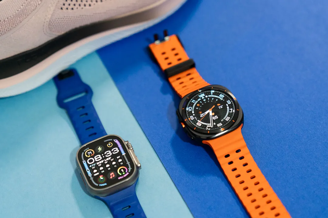 Apple Watch Ultra 2 与三星 Galaxy Watch Ultra 并排摆放，背景是一只粉色运动鞋