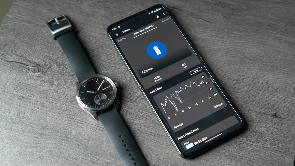 Withings ScanWatch 2 放在手机旁边，手机上已打开 Withings 应用程序进行锻炼。