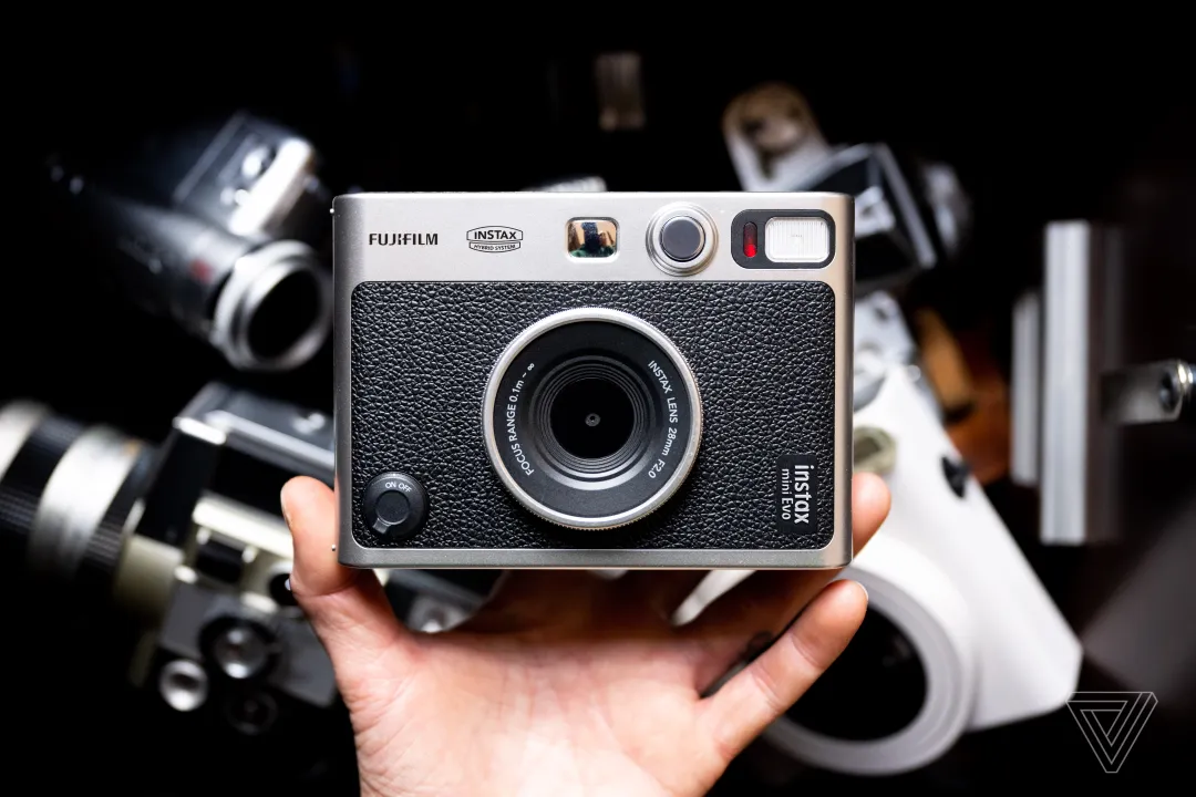 一只手拿着 Instax Mini Evo，背景是黑暗的，相机没有对焦。