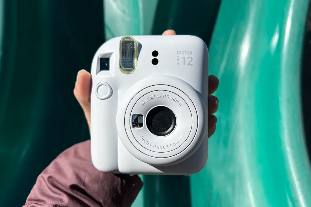 一只手将白色的 Fujifilm Instax Mini 12 举在绿色幻灯片上。