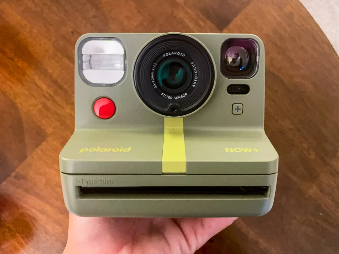 在棕色背景下，绿色第二代 Polaroid Now Plus 的特写。