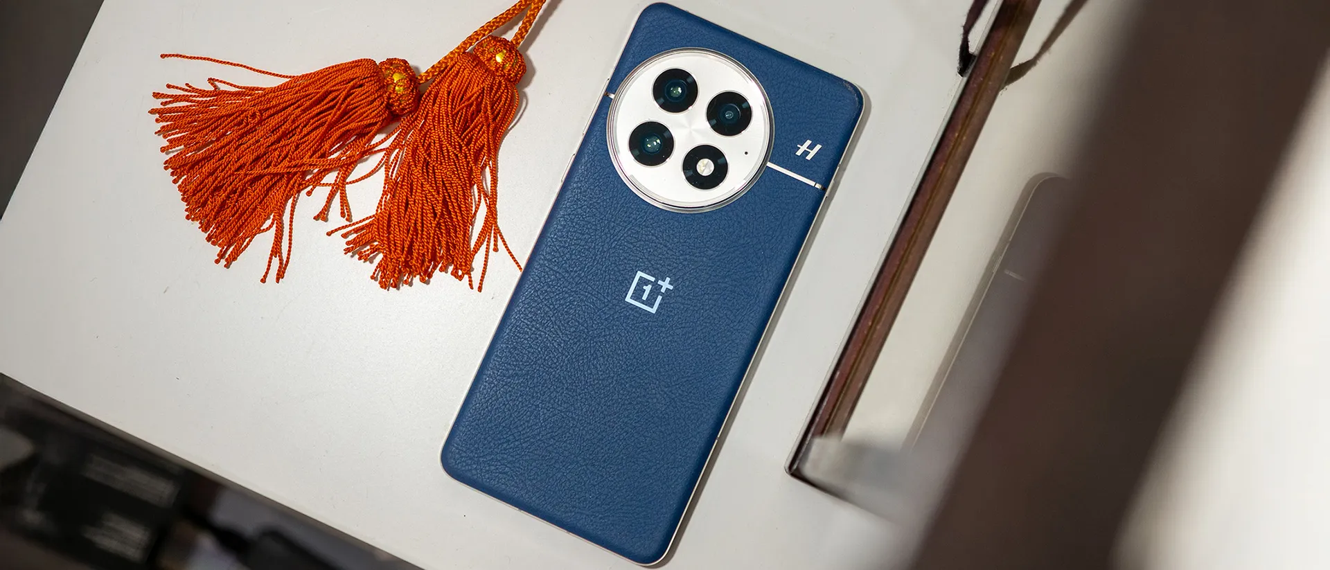 蓝色 OnePlus 13 的背面，旁边是一些橙色流苏