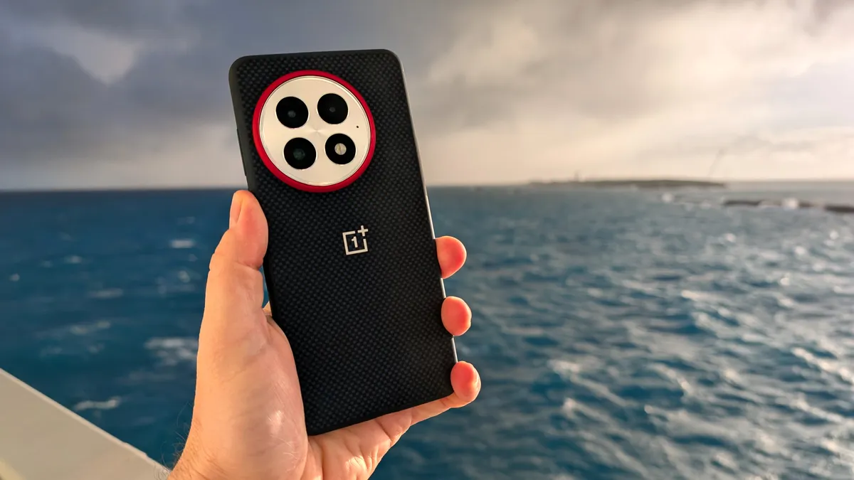 拿着装在蓝色保护壳里的 OnePlus 13，背景是大海