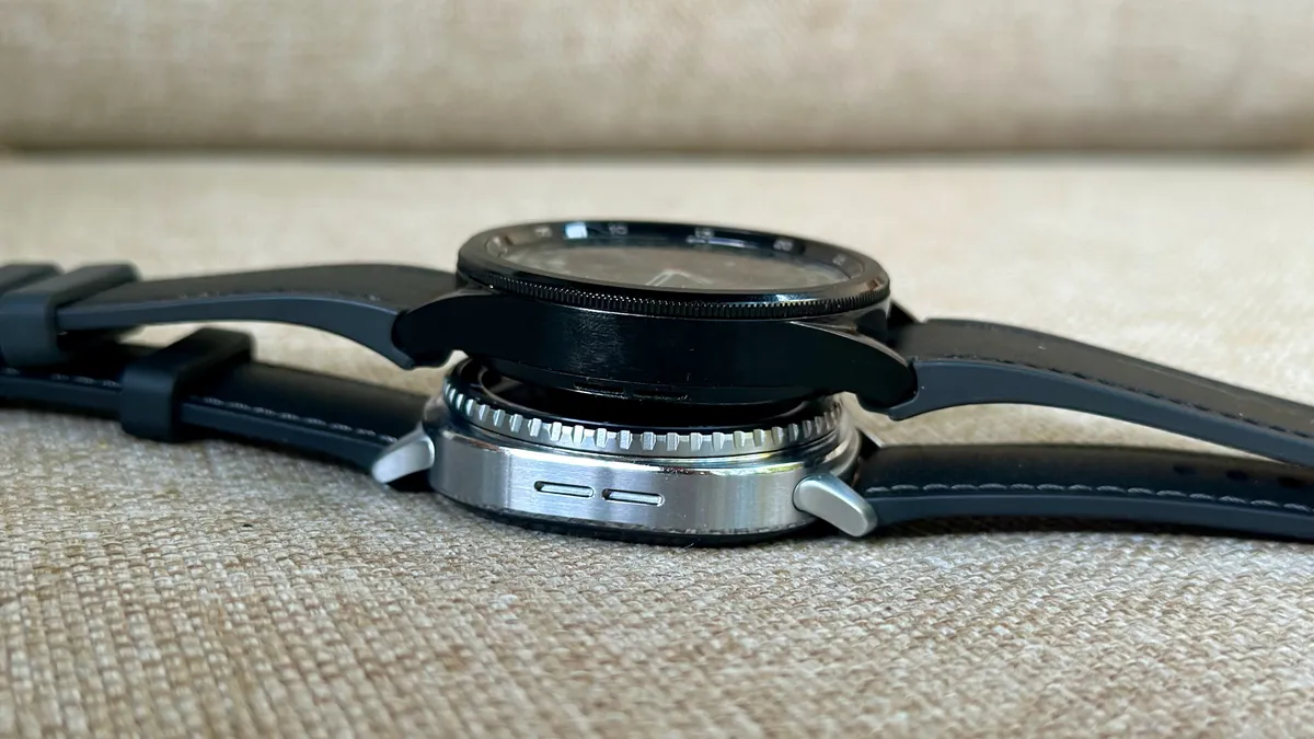 三星 Galaxy Watch 6 Classic（上）位于三星 Galaxy Watch 6 Classic（下）上方，照片以一定角度显示它们的厚度以及曲面 6 表壳和平面 8 表壳之间的差异。