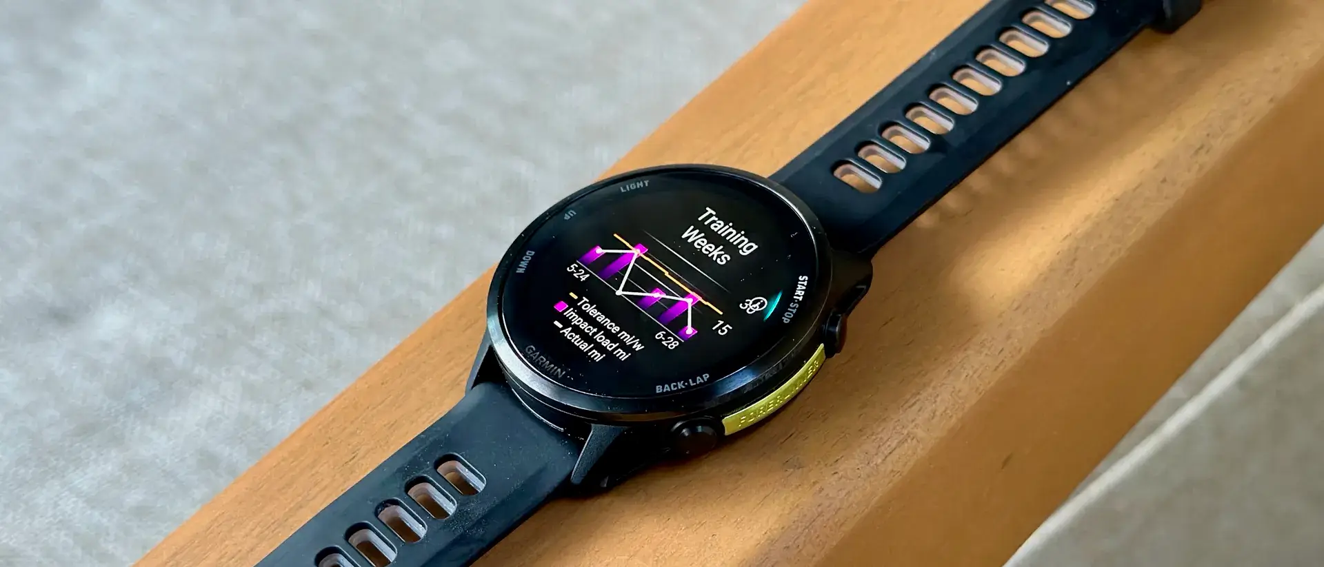 Garmin Forerunner 970 放在扶手上，显示训练周数小部件，其中包含四周的冲击负荷里程和跑步耐受力数据。