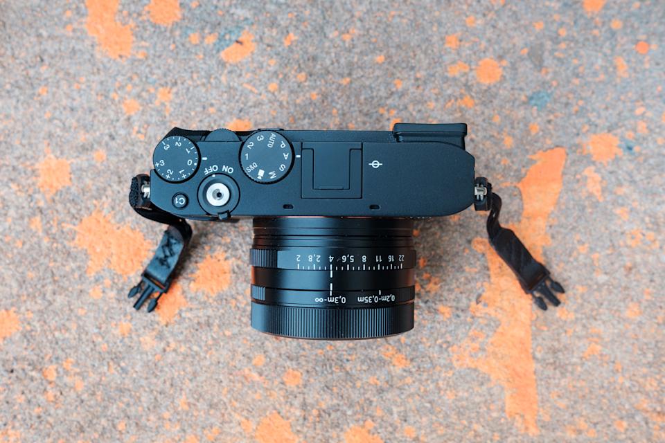 RX1R III 的俯视图，展示了相机的顶部拨盘。它放置在溅有橙色油漆的混凝土上。