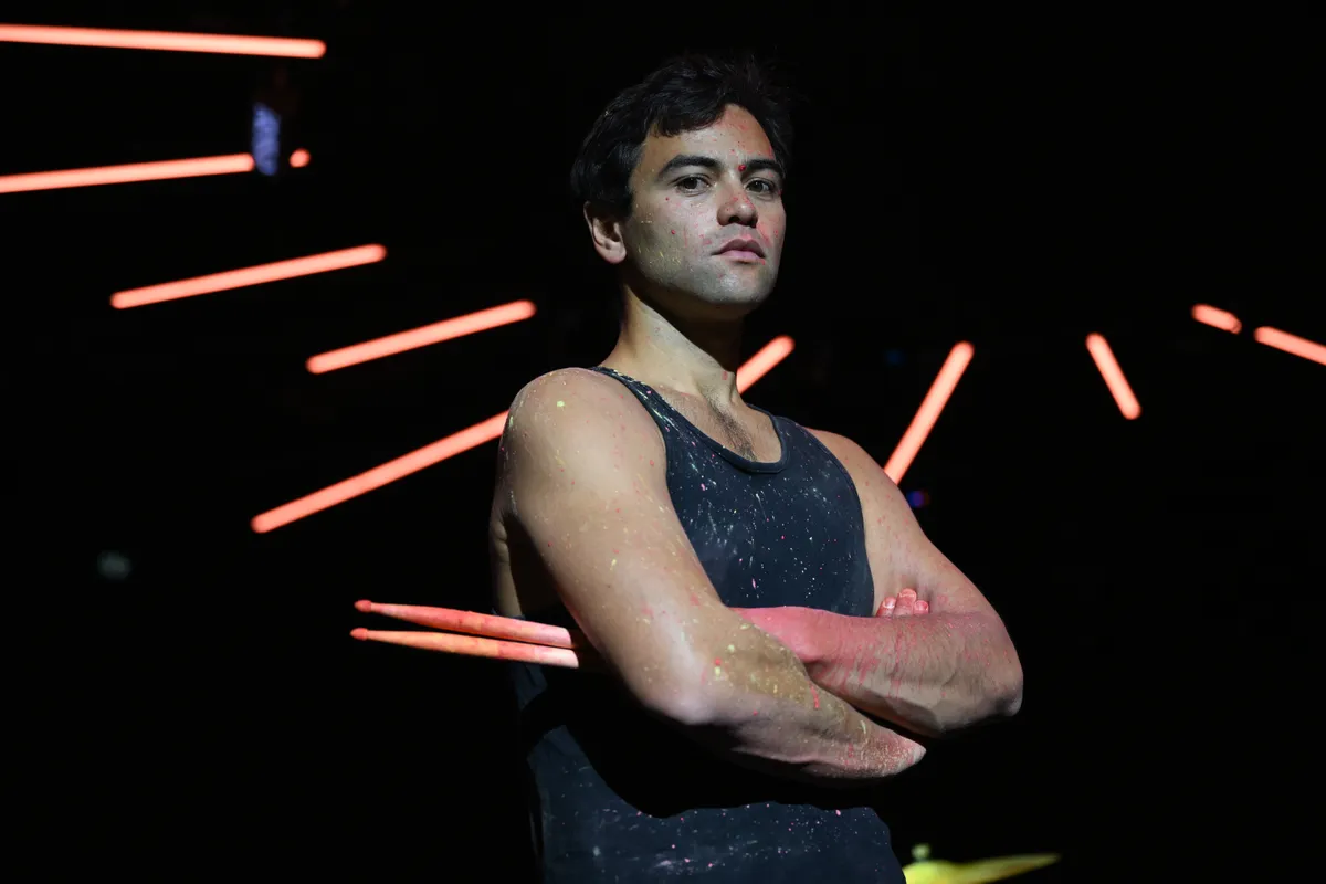 黑暗工作室里的一名男鼓手，双臂交叉，手握鼓棒，背景是霓虹灯