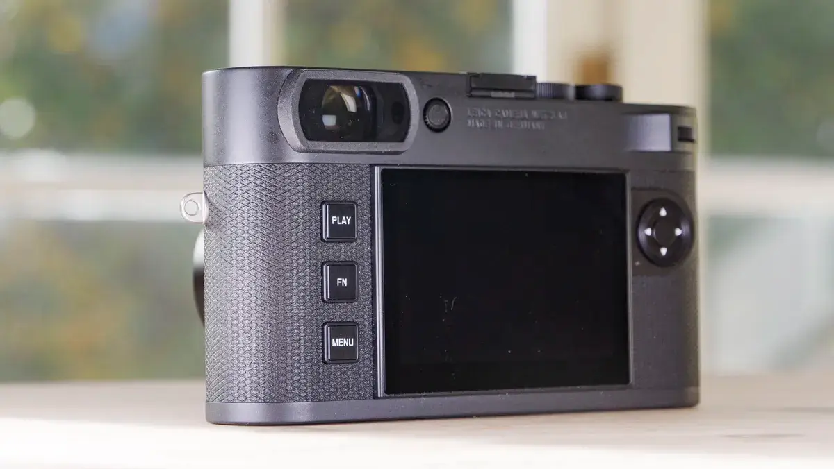 徕卡 M EV1 相机的背面，放在一张木桌上，背景是玻璃门