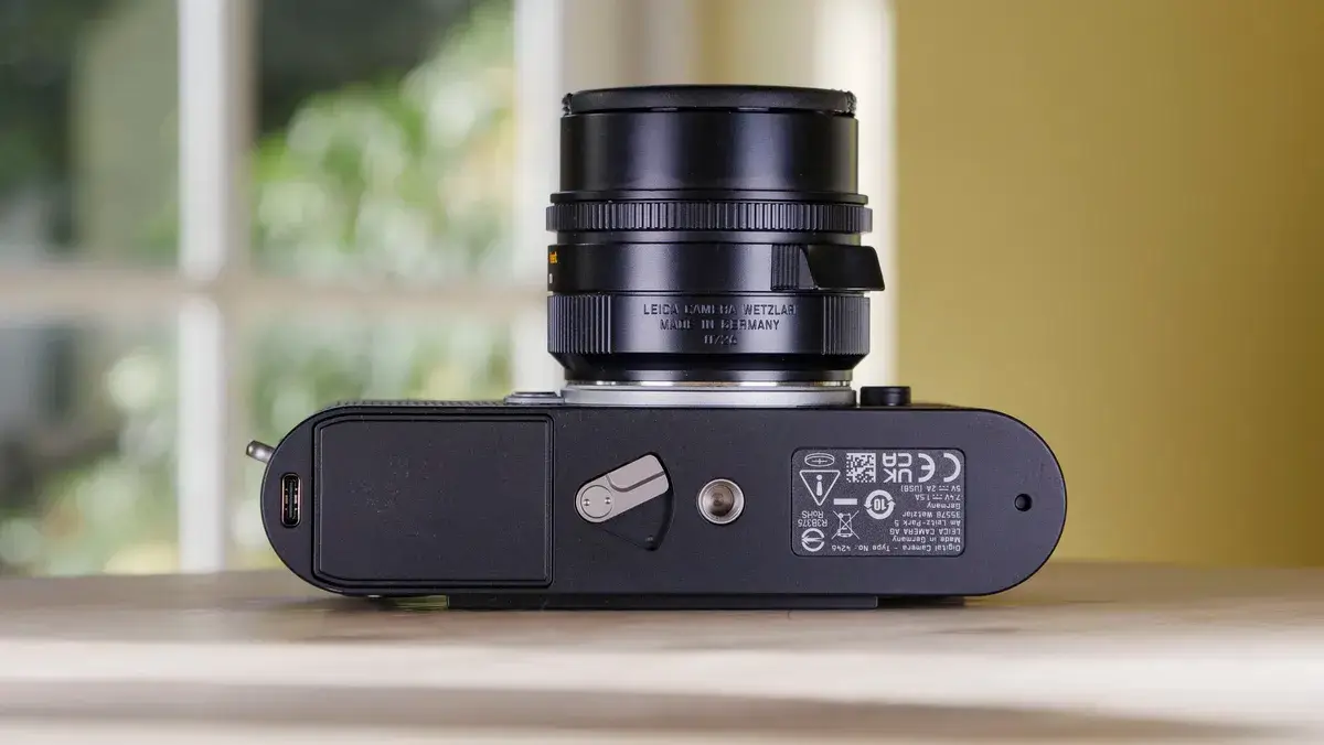 徕卡 M EV1 相机的底面，放在带有玻璃门背景的木桌上
