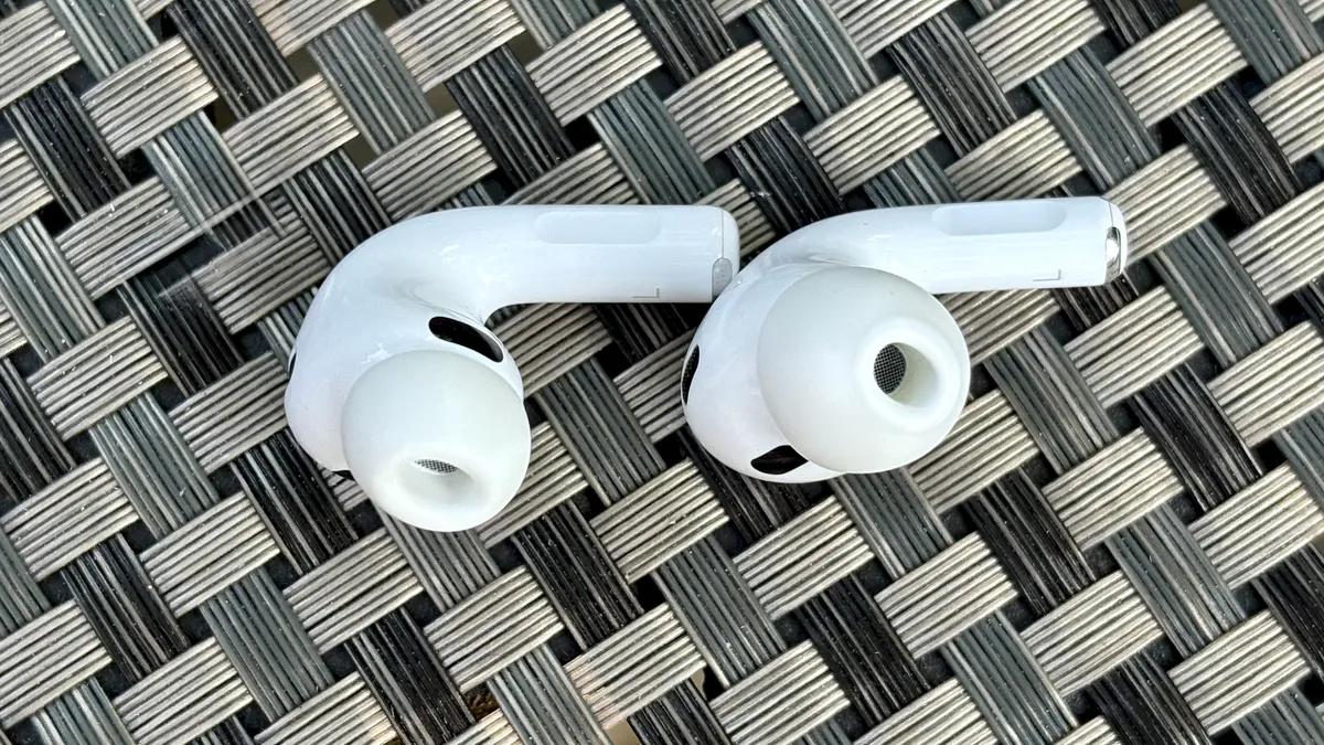一名男子戴着 Apple AirPods Pro 3 站在红砖墙前，或将其放在带灰色麻绳套的桌子上