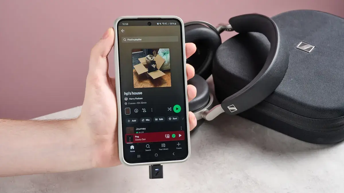 一个人在 Sennheiser HDB 630 和便携包前举着打开 Spotify 的手机