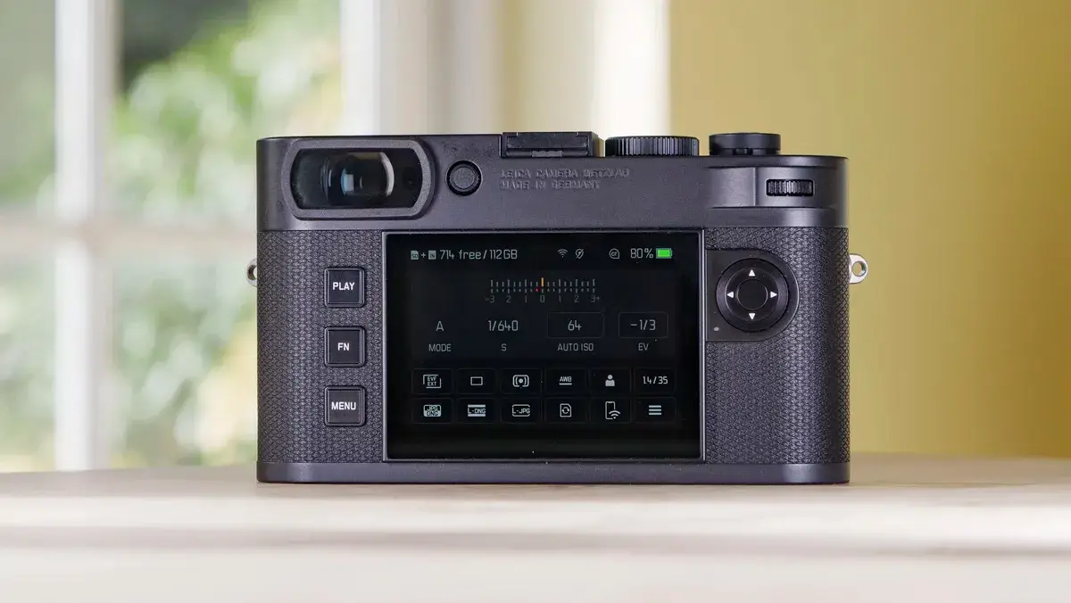 徕卡 M EV1 相机的后屏幕放在木桌上，背景是玻璃门