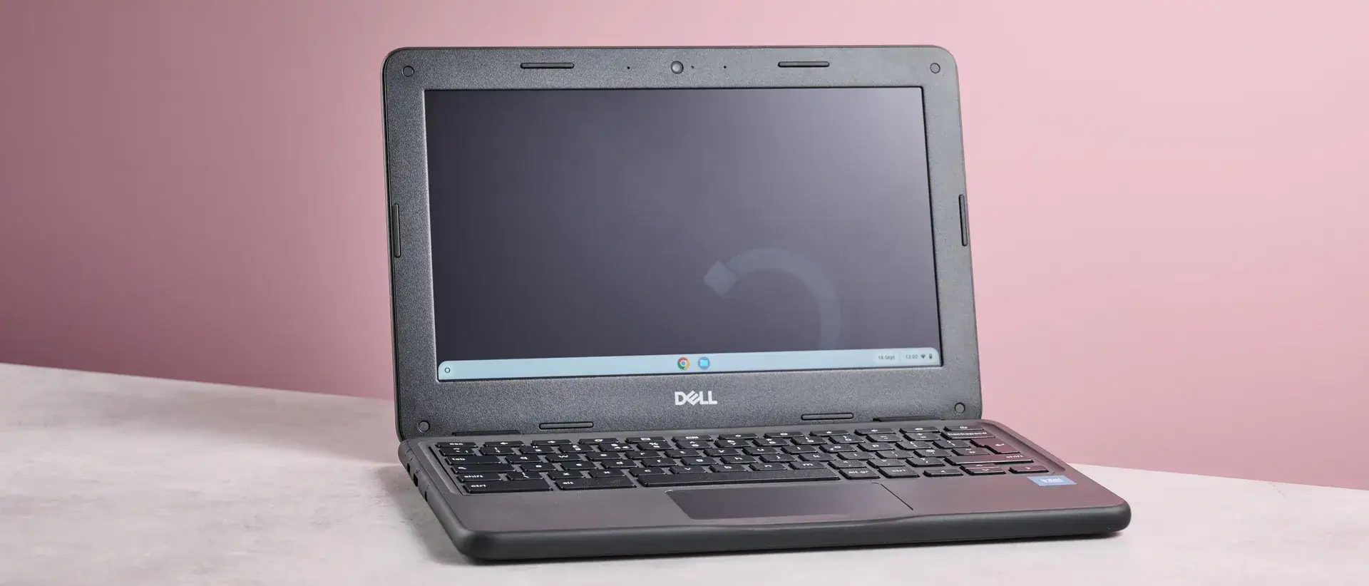 桌面上打开的戴尔 Chromebook 3120，背景是粉色墙壁，视角为四分之三。
